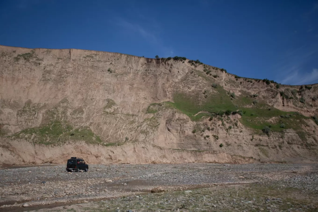 Высокий берег реки Оби-Мазар, высота проведения раскопок – 50-70 метров от уровня реки. УАЗик везет нас прямо по реке. Фото Алексея Паевского.