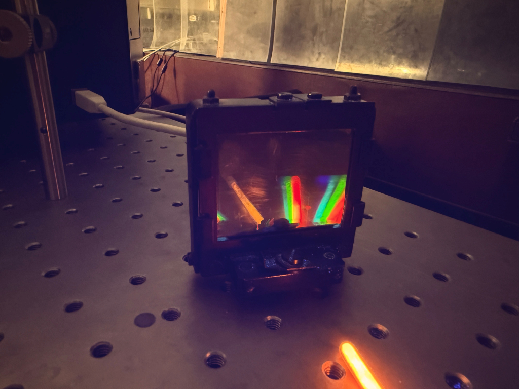 Дифракционная картина люминесценции исследуемого вещества. Видно, как оранжевое свечение самого образца раскладывается на отдельные цветовые компоненты в результате дифракции